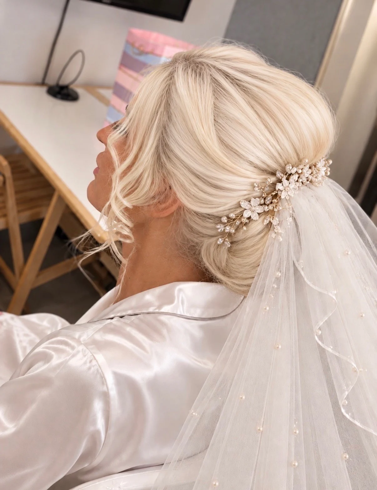 A softly swept blonde bridal updo finished with pearl flowers and a veil, created by Amber